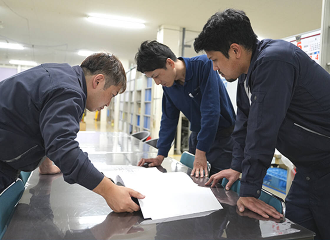 机の上に書類を広げて打ち合わせを行う3人の男性